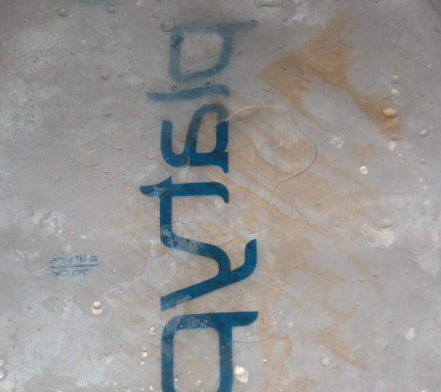 A close-up photo of a translucent surface from hydration systems with the word plastic printed in blue, appearing upside down and partially obscured by water droplets and smudges, highlighting the importance of preventing mold.