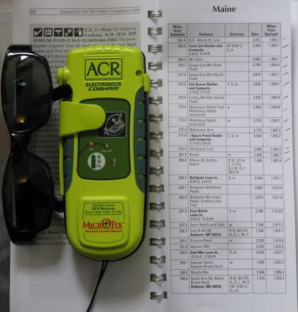 A pair of black sunglasses and a green ARC MicrOFix Personal Locator Beacon rest on an open spiral-bound directory, displaying a list of radio frequencies and services for Maine.