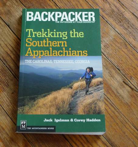 A guidebook titled Backpacker: Trekking the Southern Appalachians by Jack Igelman & Corey Hadden rests on a wooden floor, featuring a hiker trekking the Southern Appalachians along a mountain trail on the cover.
