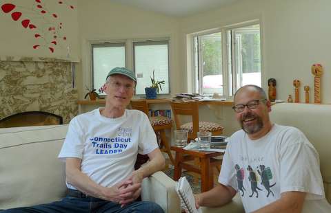 Two men sit and smile in a bright, cozy living room. One wears a Connecticut Trails Day Leader shirt and cap, while the other holds a notebook. A nod to long distance trail bootstrapping, Ron Strickland’s influence is felt in their conversation.
