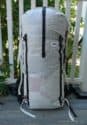 A large, white Hyperlight Mountain Gear 4400 Porter Pack ultralight backpack with black straps and hip belt sits upright on a wooden porch, with a white railing and greenery in the background—ready for any expedition.