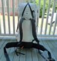 A white Hyperlight Mountain Gear 4400 Porter Pack with black straps and a padded hip belt stands upright on a wooden porch, framed by vertical white railings and houses in the background, ready for your next expedition.