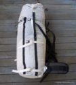 A white Hyperlight Mountain Gear 4400 Porter Pack ultralight backpack with black straps and a padded hip belt sits on a wooden deck, ready for your next expedition, viewed from above.