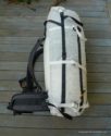 A Hyperlight Mountain Gear 4400 Porter Pack, featuring black straps and buckles, sits upright on a wooden deck, showcasing its padded shoulder straps, hip belt, and back panel—perfect for your next expedition.